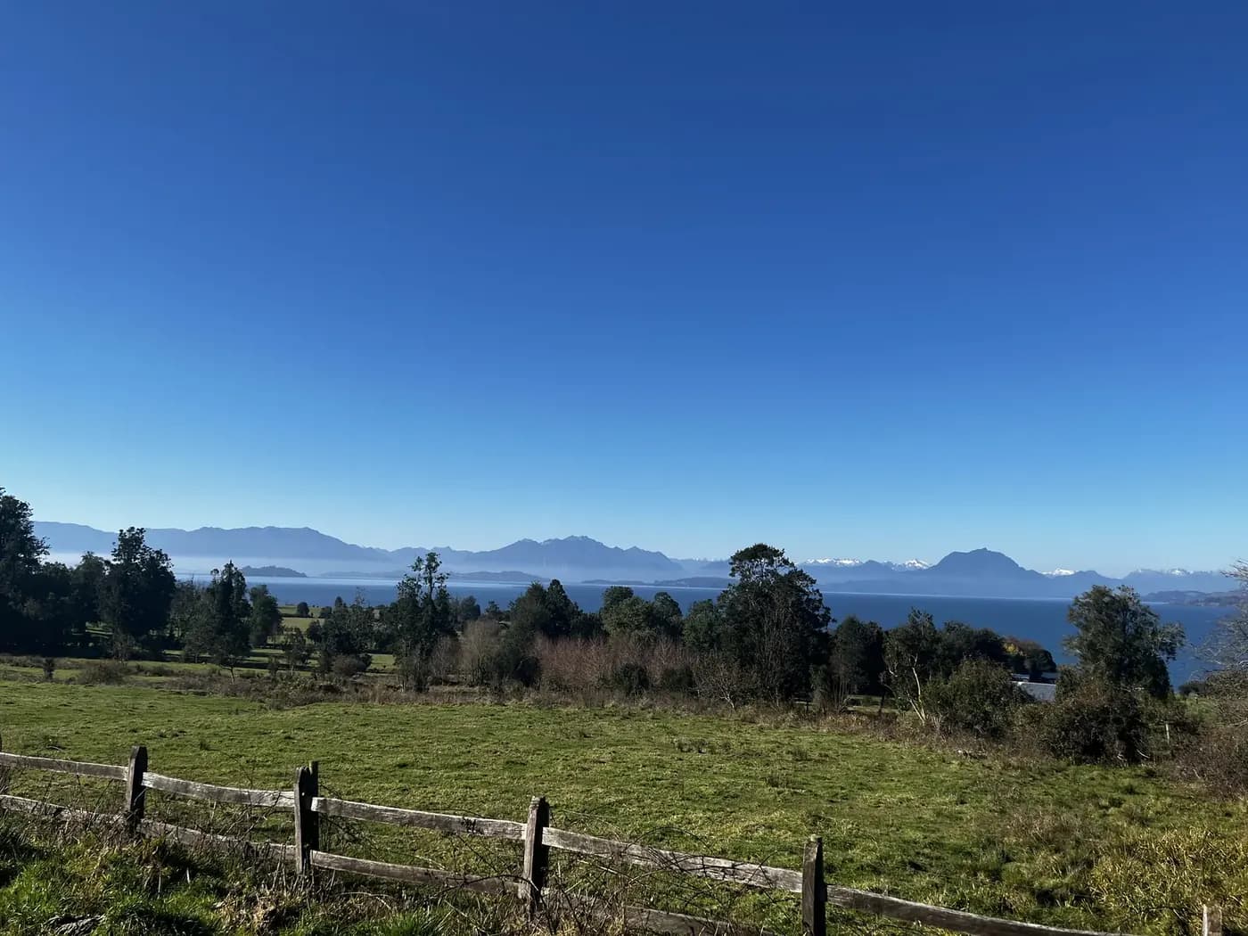 Cerco de madera sobre la pradera, con el lago Ranco y los cerros al fondo