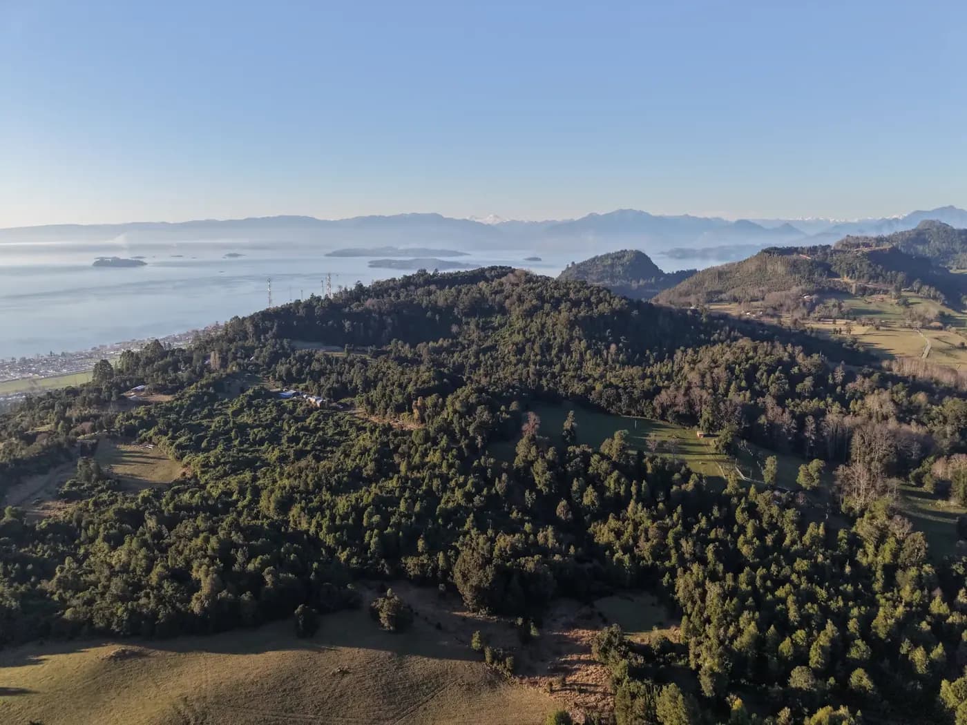 Vista aérea de los cerros del predio con el lago y la cordillera al fondo